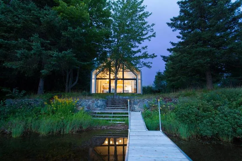 W ciemności dom nad brzegiem jeziora, dzięki dużym oknom, odbija się dużą jasną gwiazdą.