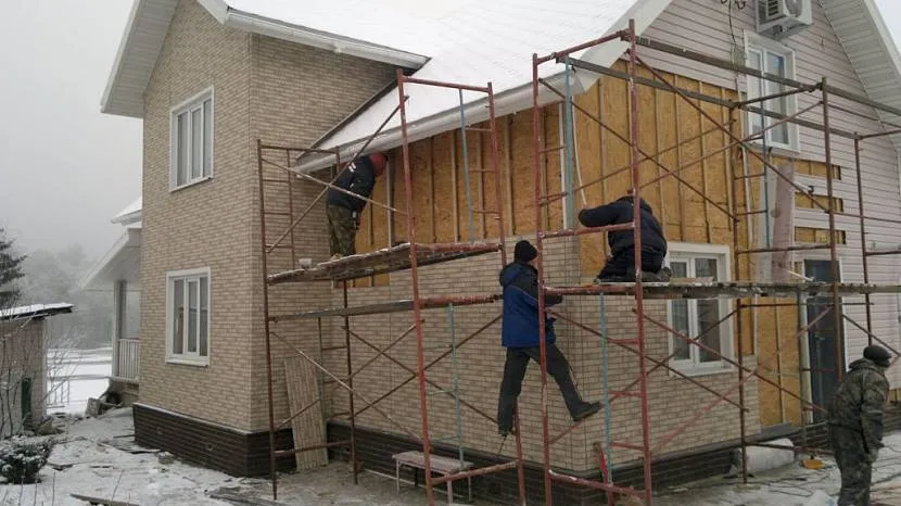 Комбіноване зовнішнє облицювання будинку пластиковими панелями з імітацією цегляної кладки та вініловим сайдингом бежевого кольору.