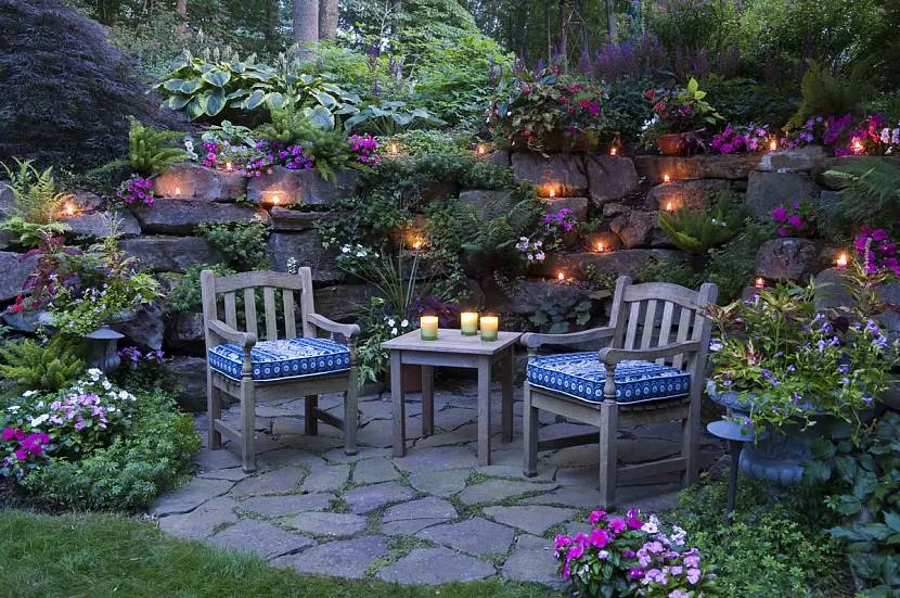 Malowniczy zakątek do wypoczynku w ogrodzie z pięknym oświetleniem na kamiennym ogrodzeniu