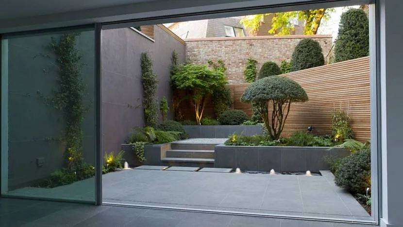 Маленький сад, оформлений у японському стилі з бонсаї, хвойниками та сірою плиткою