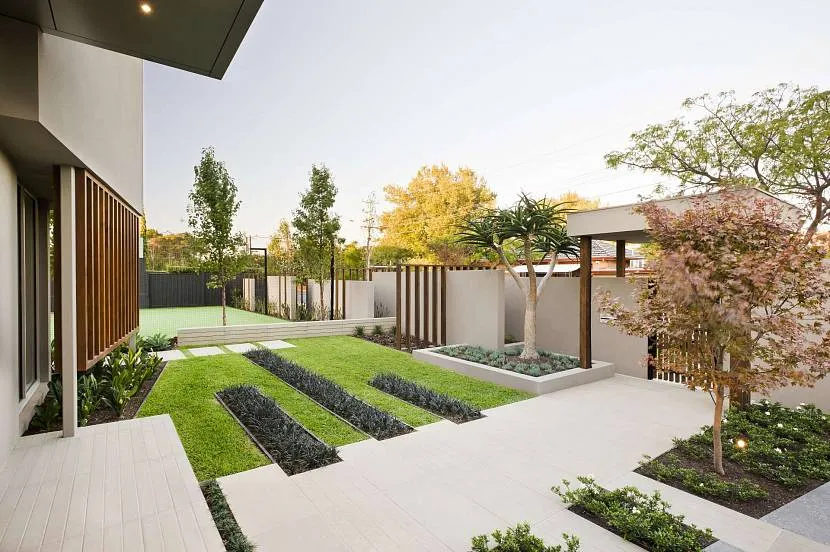 Frontowy ogród z geometrycznymi klombami, szeroką ścieżką i szarym ogrodzeniem